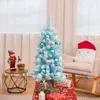 A decorated mini Christmas tree with presents underneath, placed in a living room setting with a rocking chair and decorative figures. Podgląd zdjęcia produktu