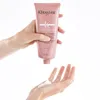 A person is squeezing a pink tube of conditioner into their hand. Podgląd zdjęcia produktu