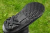 Close-up of the sole of a black boot against a blurred green grassy background. Produktbild-Vorschau