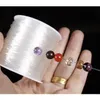 A hand holding a spool of white elastic cord with several beads threaded onto it. Anteprima dell’immagine prodotto