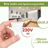 A hand holding a GU5.3 LED lamp with a living room in the background. Produktbild-Vorschau