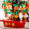 A close-up view of a LEGO model of a lucky chestnut tree, decorated with small orange pumpkins, red envelopes, and gold coins. Produktbild-Vorschau