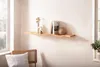 A wooden shelf with decorative items on it, placed on a wall next to a window and a chair. Produktbild-Vorschau