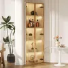 A tall, narrow display cabinet with glass doors and LED lighting, showcasing various items on its shelves. A potted plant stands to the left, and a small round table with a vase of flowers is to the right. Produktbild-Vorschau