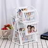 A white Ferris wheel photo frame sits on a checkered surface, with a basket of flowers to the left and a book to the right. Voir les images du produit
