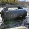 A black portable speaker is submerged in water, with splashes around it, suggesting it is waterproof and durable. Náhled obrázku produktu