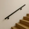 A black metal handrail is mounted on a light beige wall next to wooden stairs. Náhľad obrázku produktu