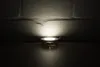 A small LED light is illuminated on a dark surface, casting a bright light onto a textured white brick wall. Produktbild-Vorschau