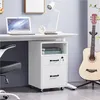 A white filing cabinet with two drawers and an open shelf is shown next to a desk with a laptop and a lamp. A guitar is also visible in the background. Produktbild-Vorschau