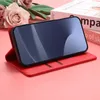 A red phone case with a phone inside is displayed on a pink surface, with flowers in the background. Produktbild-Vorschau