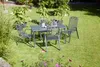 A garden dining set with a table and four chairs is placed on a green lawn surrounded by plants and flowers. Produktbild-Vorschau