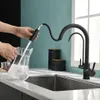 A person is filling a glass pitcher with water from a black kitchen faucet. Produktbild-Vorschau