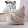 A plush snail toy sits on a light-colored surface, with a blurred background of flowers and books. Produktbild-Vorschau