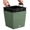 Hands holding a black insert tray with handles, placing it into a green textured planter pot. Produktbild-Vorschau