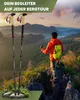A person is standing on a rocky outcrop overlooking a mountainous landscape, holding trekking poles. The trekking poles are also shown in the foreground. Produktbild-Vorschau