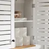 A white cabinet with louvered doors, showing shelves with toilet paper rolls and a decorative bowl. Náhled obrázku produktu