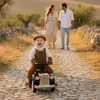 A family on a cobblestone path in a rural setting, with a baby in a toy car in the foreground. Náhled obrázku produktu