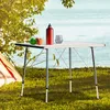 A camping table set up outdoors near a tent, with a lake and trees in the background. Produktbild-Vorschau