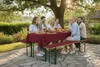 A group of six people are enjoying a meal and drinks outdoors at a picnic table under a large tree. Produktbild-Vorschau