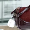 A clear case for Apple AirPods is attached to a burgundy handbag. Produktbild-Vorschau