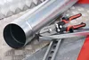 A pair of metal cutting shears rests on a piece of metal conduit, with other metal materials in the background. Anteprima dell’immagine prodotto