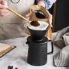 A person is preparing pour-over coffee, adding coffee grounds to a filter set over a ceramic coffee pot. Produktbild-Vorschau