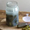 A glass jar filled with pickles and brine sits on a wooden surface, with a few pickles and slices on the side. Podgląd zdjęcia produktu