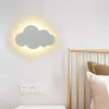 A cloud-shaped wall lamp is mounted on a white wall above a bedside table. A gold-colored headboard and pillows are visible to the right. Produktbild-Vorschau
