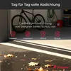 A garage interior with a bicycle, a red canister, and a green hose. The foreground shows a wet garage floor with fallen leaves. Produktbild-Vorschau