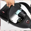 A hand is opening a black sling bag, revealing its contents. Voir les images du produit