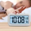 A person's hand is reaching to turn off a digital alarm clock that is displaying the time and temperature. Voir les images du produit