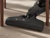 A close-up shot of a vacuum cleaner head on a wooden floor, near chair legs. Voir les images du produit
