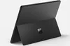 A black Microsoft Surface Pro tablet is shown from a rear-facing, slightly angled perspective, standing on its kickstand against a light gray background.