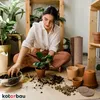 A woman is repotting plants indoors, surrounded by various plants and gardening supplies. Podgląd zdjęcia produktu