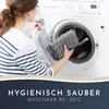 A woman is putting a gray bath mat into a washing machine. Voir les images du produit