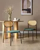 Two dining chairs with dark green seats and woven backs are placed around a wooden dining table in a room with a painting on the wall. Náhled obrázku produktu