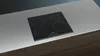 A black induction cooktop with four burners is shown on a light gray countertop. Produktbild-Vorschau
