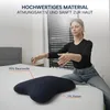 A woman is sitting on a bed next to a pillow, demonstrating its features. Produktbild-Vorschau