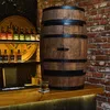 A wooden barrel-shaped cabinet with a glass of whiskey on a wooden bar counter, with bottles on shelves in the background. Produktbild-Vorschau