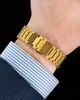 A close-up shot of a gold watch bracelet on a person's wrist, with a blue and white striped shirt cuff visible. Anteprima dell’immagine prodotto