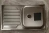 A stainless steel sink with a drainboard is shown from a top-down view, lying on a textured surface. Produktbild-Vorschau