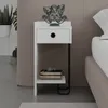 A white bedside table with a drawer and a shelf, next to a bed. There is a decorative dog figurine on top of the table.