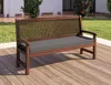 A wooden bench with a gray cushion is placed on a wooden deck outdoors, with grass and a building in the background. Produktbild-Vorschau
