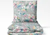 A folded bedding set and a pillow with a floral and bird pattern on a gray background. Produktbild-Vorschau