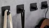 Four black adhesive hooks mounted on a gray wall, each holding a different item. Anteprima dell’immagine prodotto