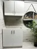 A white cabinet unit with two doors below a wall-mounted cabinet with two doors, set against a wood-paneled wall. A round mirror with a triangular frame hangs on the wall to the right, reflecting a warehouse interior. A potted plant with green foliage is i Voir les images du produit