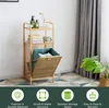 A bamboo shelving unit with a laundry basket is shown, set against a neutral background with decorative flooring. Produktbild-Vorschau