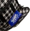 A close-up view of the inside of a black and white houndstooth patterned bag, showing a blue packet of tissues. Produktbild-Vorschau