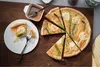 A quiche with asparagus and goat cheese is sliced on a wooden board, with a slice on a plate and a small dish of sauce. Produktbild-Vorschau