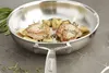 A close-up shot of a stainless steel frying pan with two pieces of cooked meat and some chopped vegetables inside, garnished with herbs. The pan is placed on a marble countertop with some scattered herbs around it. Voir les images du produit